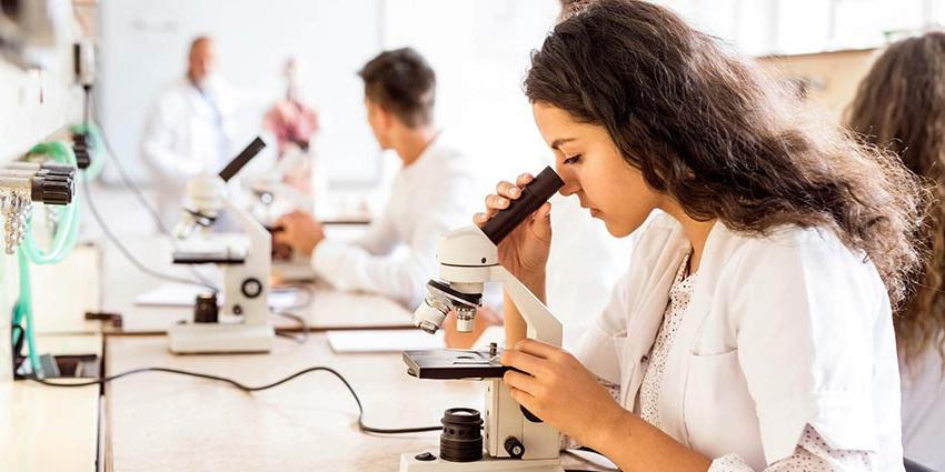 A student looking into a microscope while earning her biology degree in CT